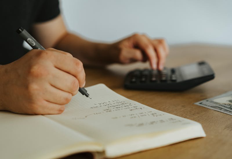 Un homme note des choses sur un calpin, et une calculatrice à côté.