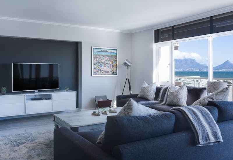 L'inrérieur d'un appartement, coin salon gris et blanc, vue sur la mer et montagne par la fenêtre.